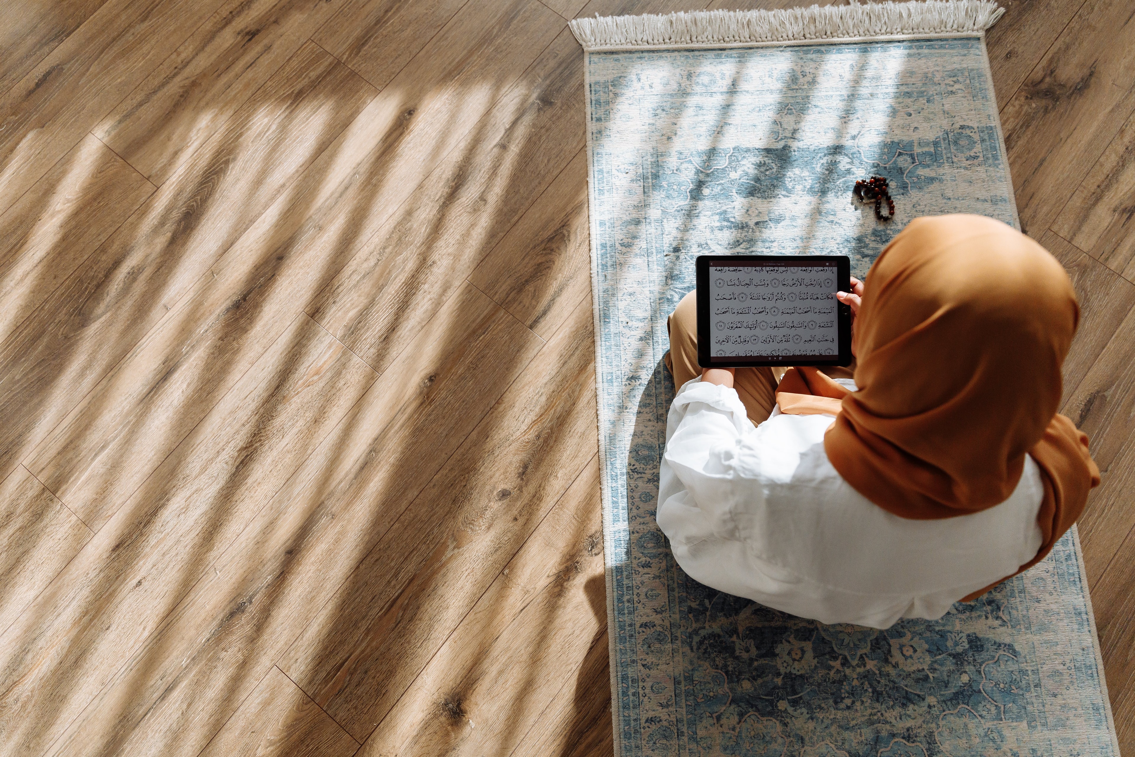 Student learning Quran online on prayer mat with tablet